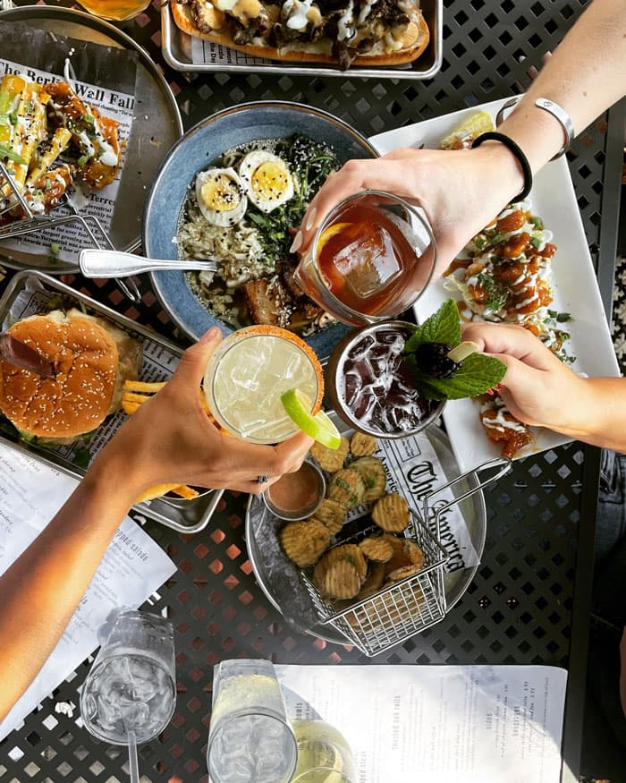 guests doing a cheers with cocktails over a patio table full of food